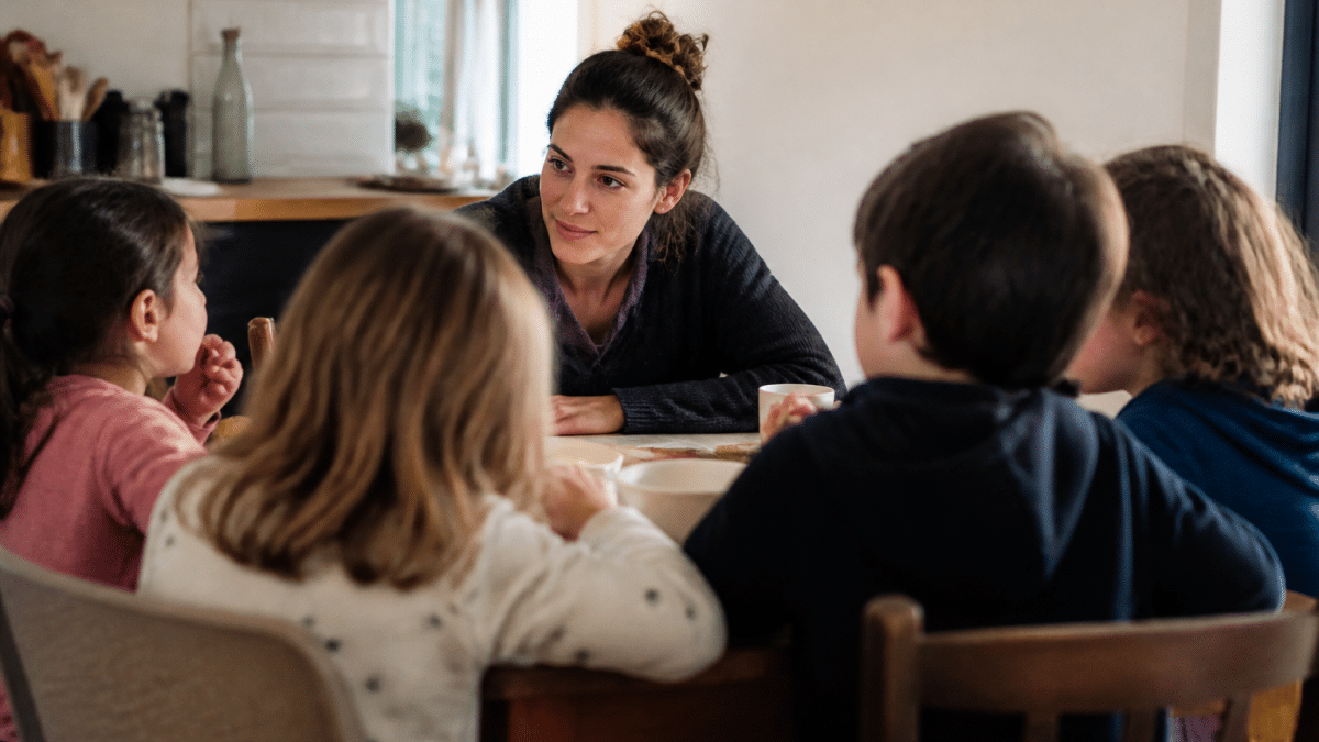 Adulte assis face a plusieurs enfants autour table