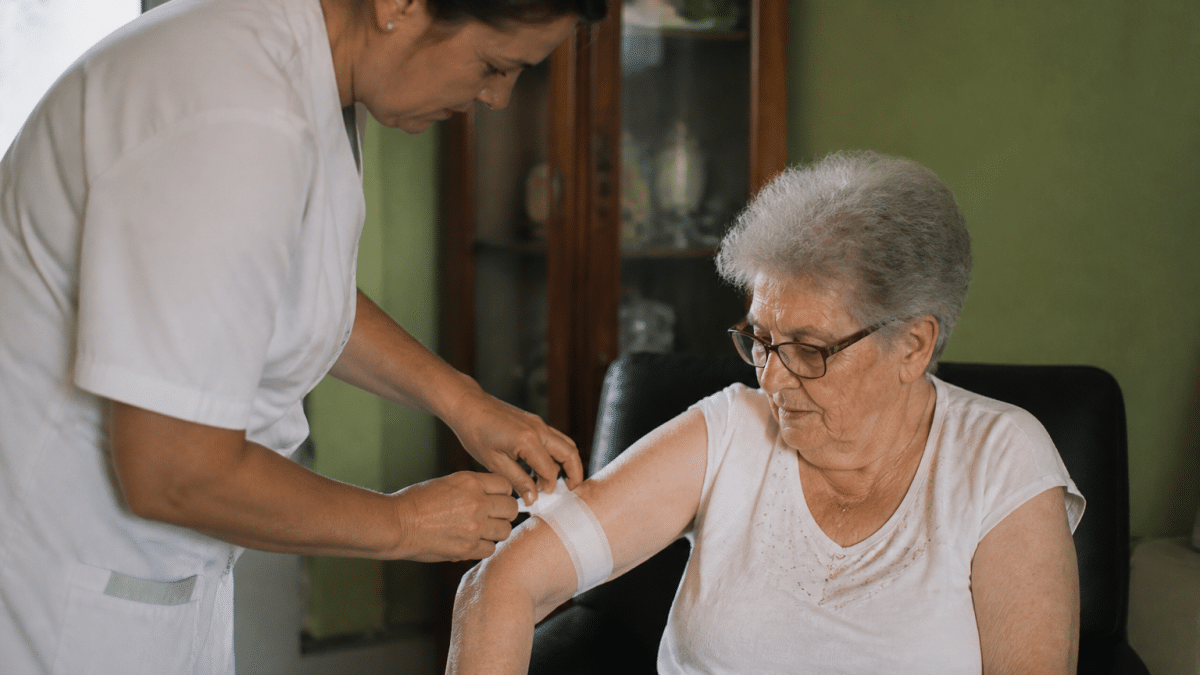 Personne agee assise recevant aide medicale d'un soignant debout
