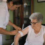 Personne agee assise recevant aide medicale d'un soignant debout