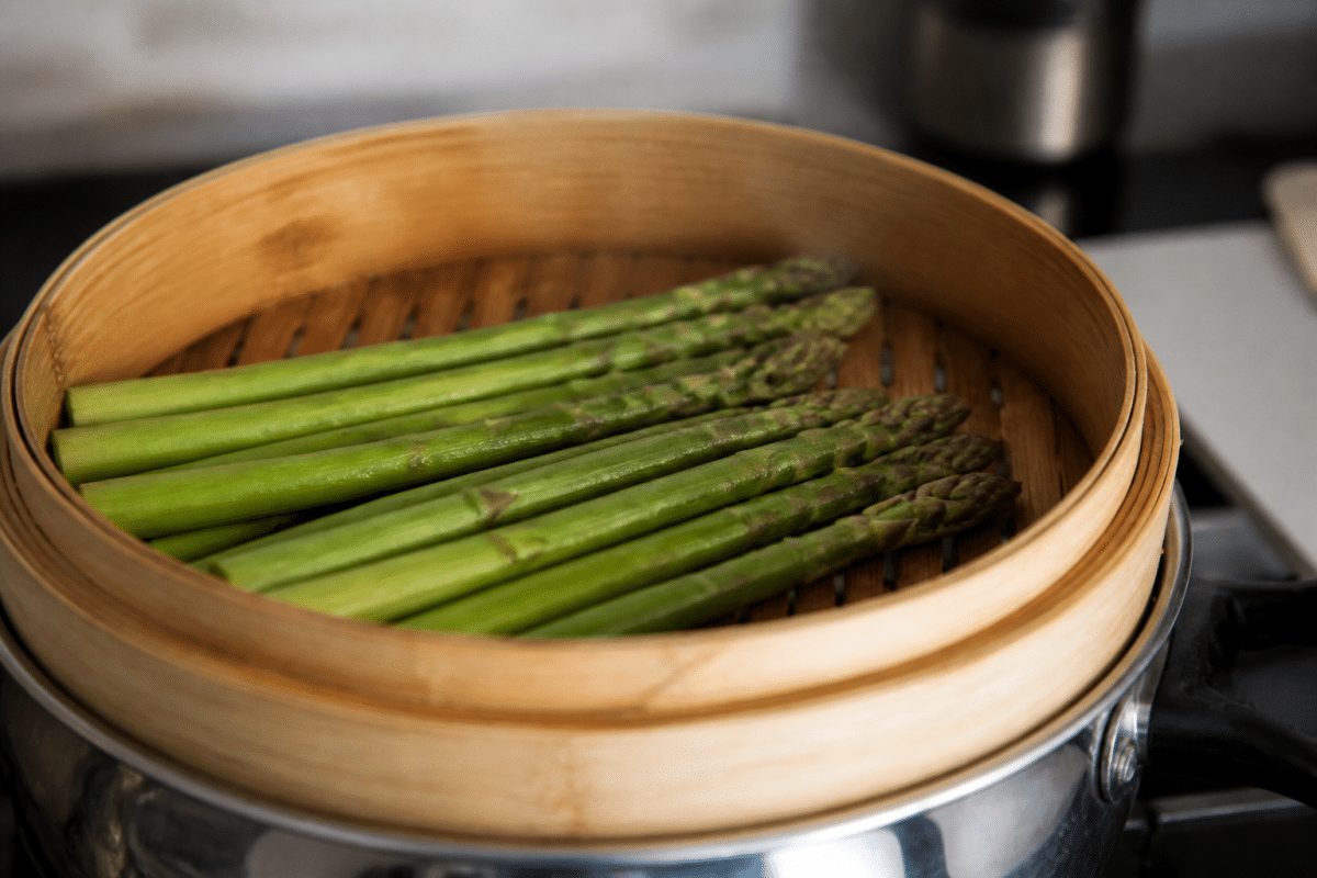 Asperges vertes dans panier vapeur au-dessus eau bouillante