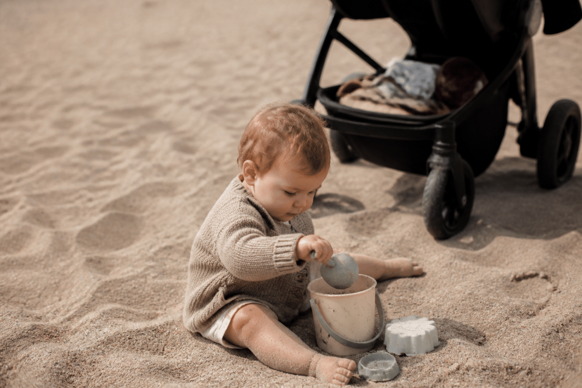 Bébé jouant dans le sable près d'une poussette