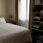 Chambre organisee avec lit fait, vetements plies sur etagere