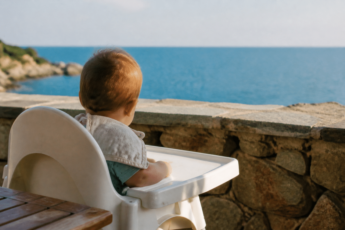 Bébé assis dans chaise haute face mer méditerranée bleue