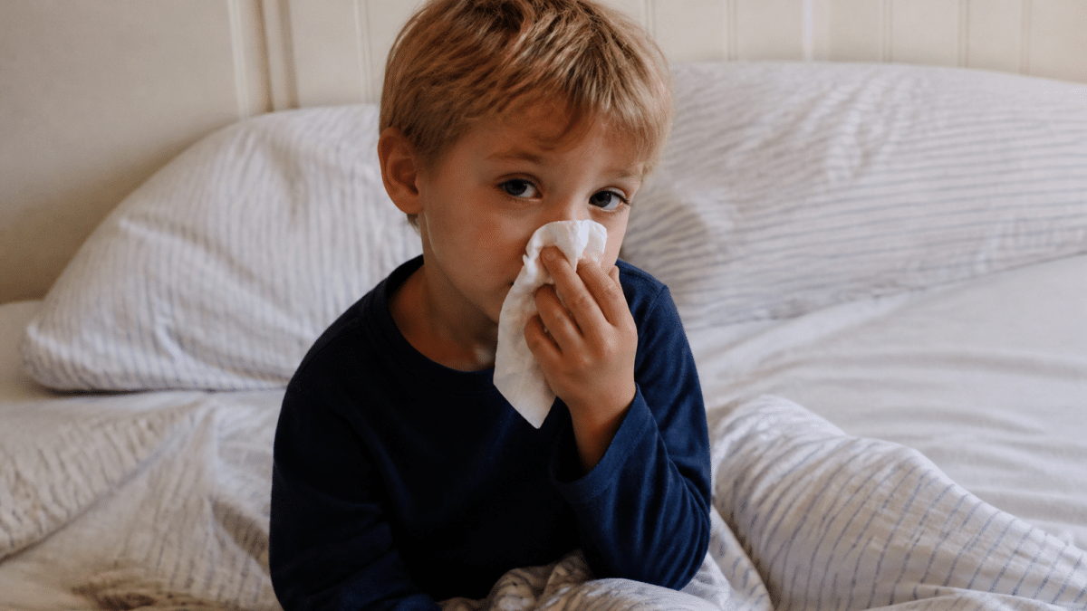 Enfant assis au lit tenant un mouchoir, visage fatigue