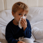 Enfant assis au lit tenant un mouchoir, visage fatigue