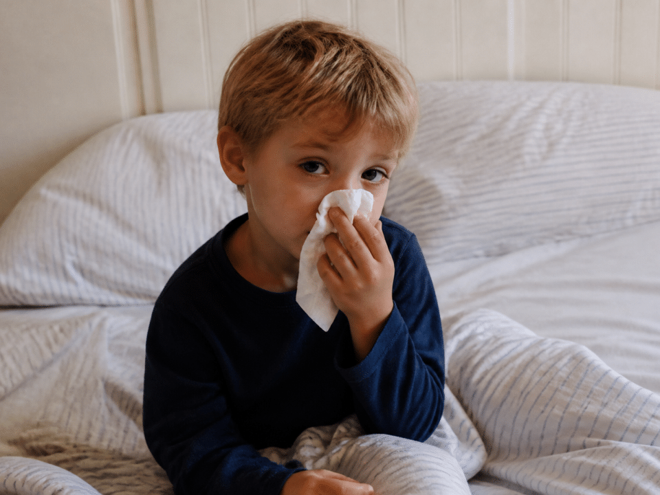 Enfant assis au lit tenant un mouchoir, visage fatigue