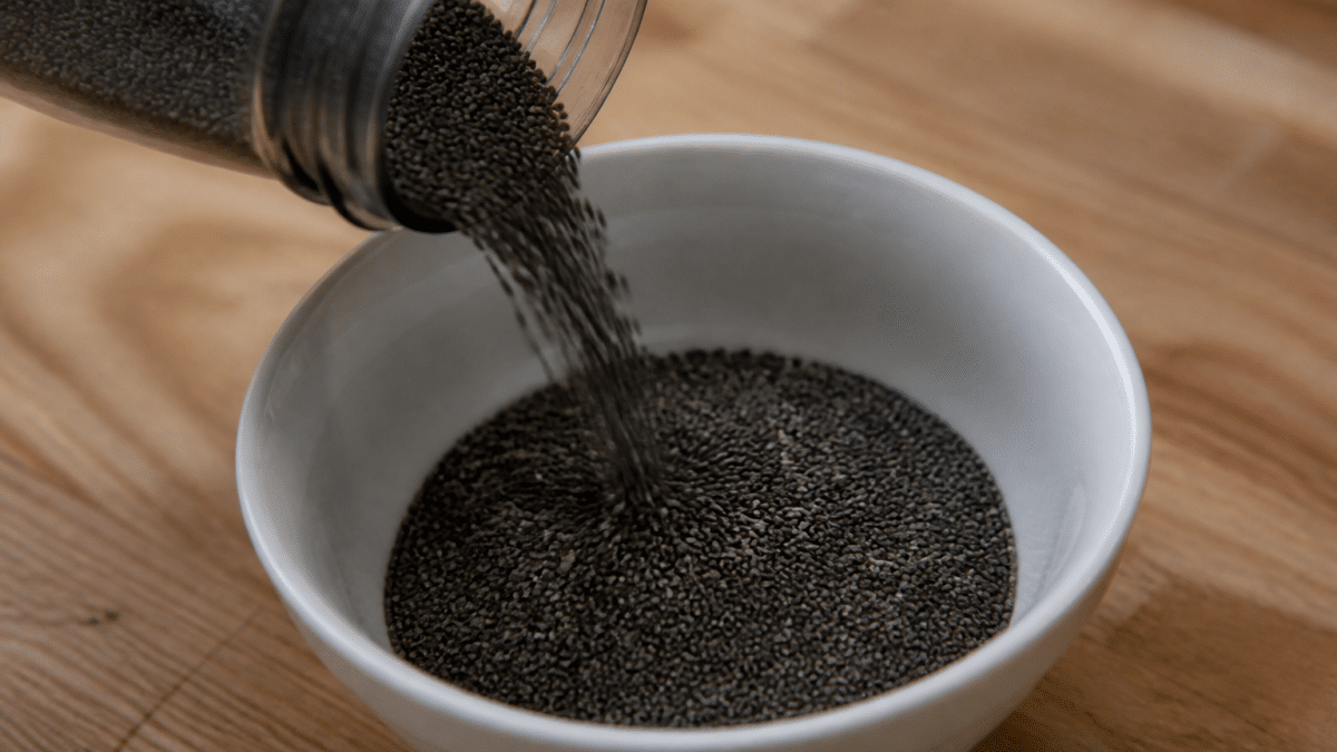 Graines de chia noires versees dans un bol blanc pose sur table