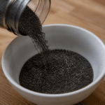 Graines de chia noires versees dans un bol blanc pose sur table