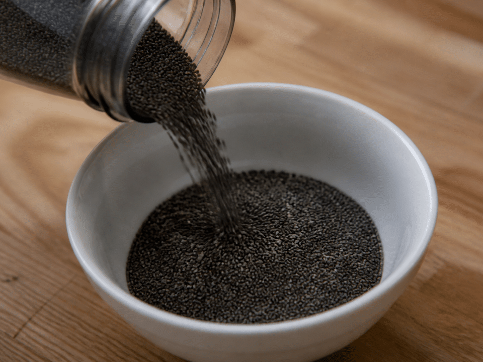 Graines de chia noires versees dans un bol blanc pose sur table