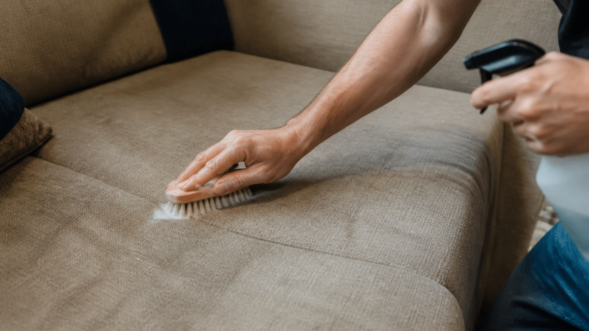 Personne frottant tissu canape avec brosse et produit nettoyant