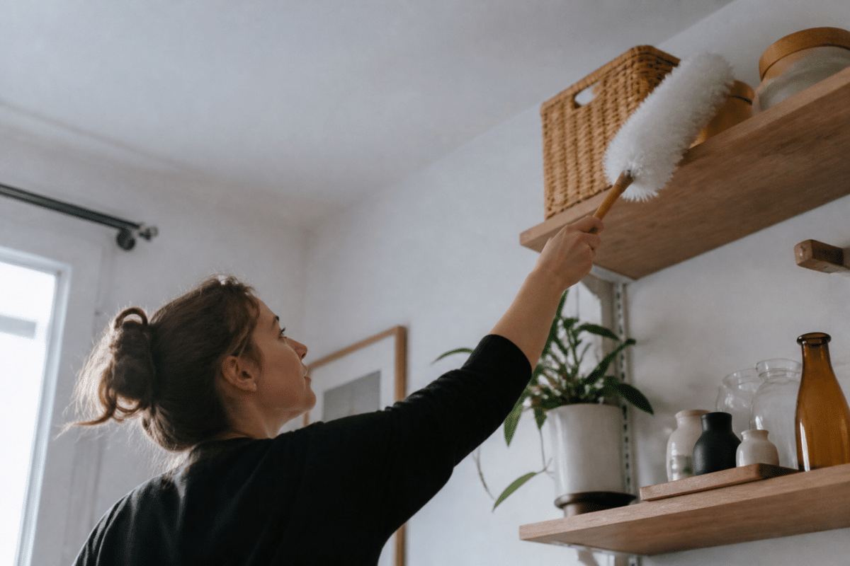 Personne nettoyant étagère haute avec plumeau blanc