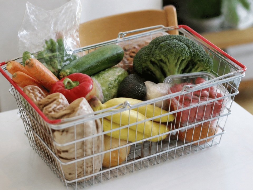 Panier d'epicerie rempli d'articles alimentaires sur table blanche