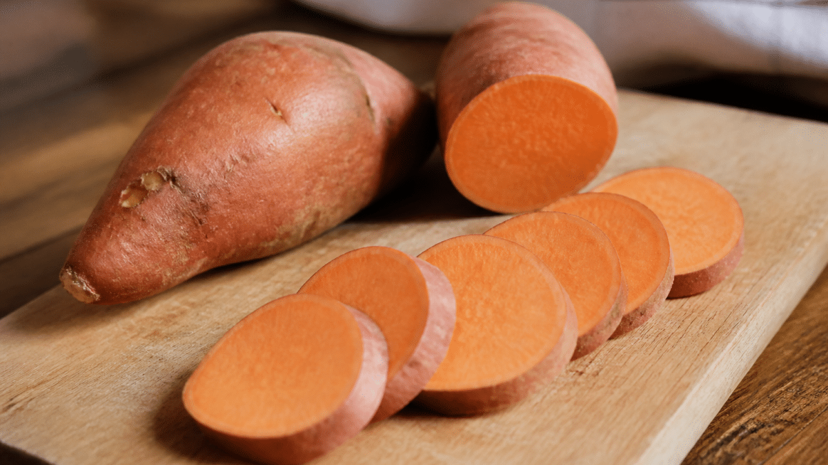 Patate douce entiere et tranchee sur planche bois