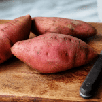 Patates douces entières posees sur planche bois, couteau a cote