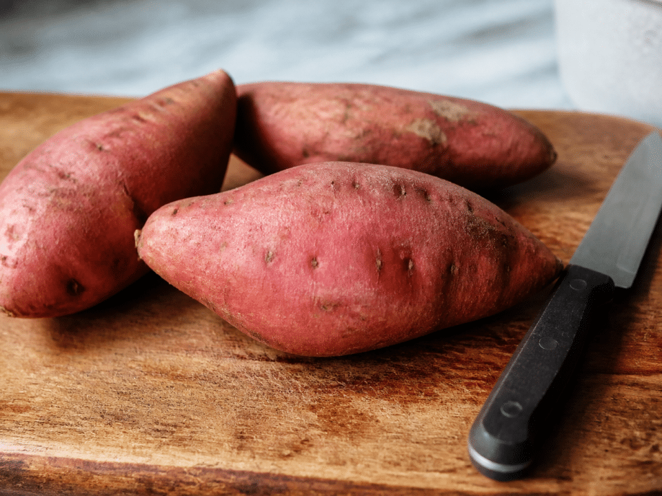 Patates douces entières posees sur planche bois, couteau a cote